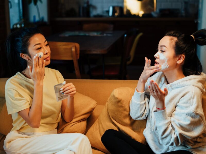 women sitting beside each other, applying skin care