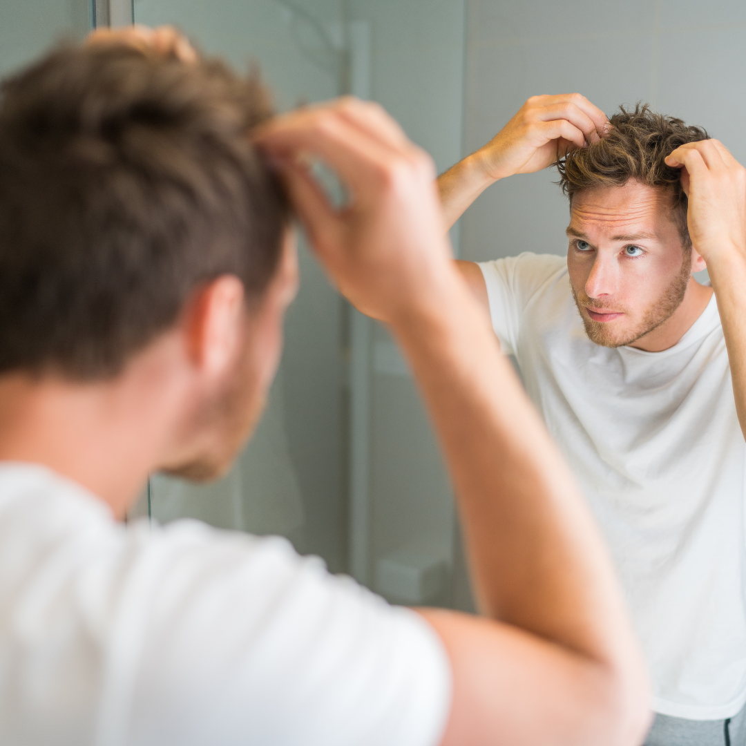 man looking at his hairline in a mirror